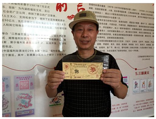一位手里举着一张用塑料膜包裹住的彩票和宣传展板合影的彩民